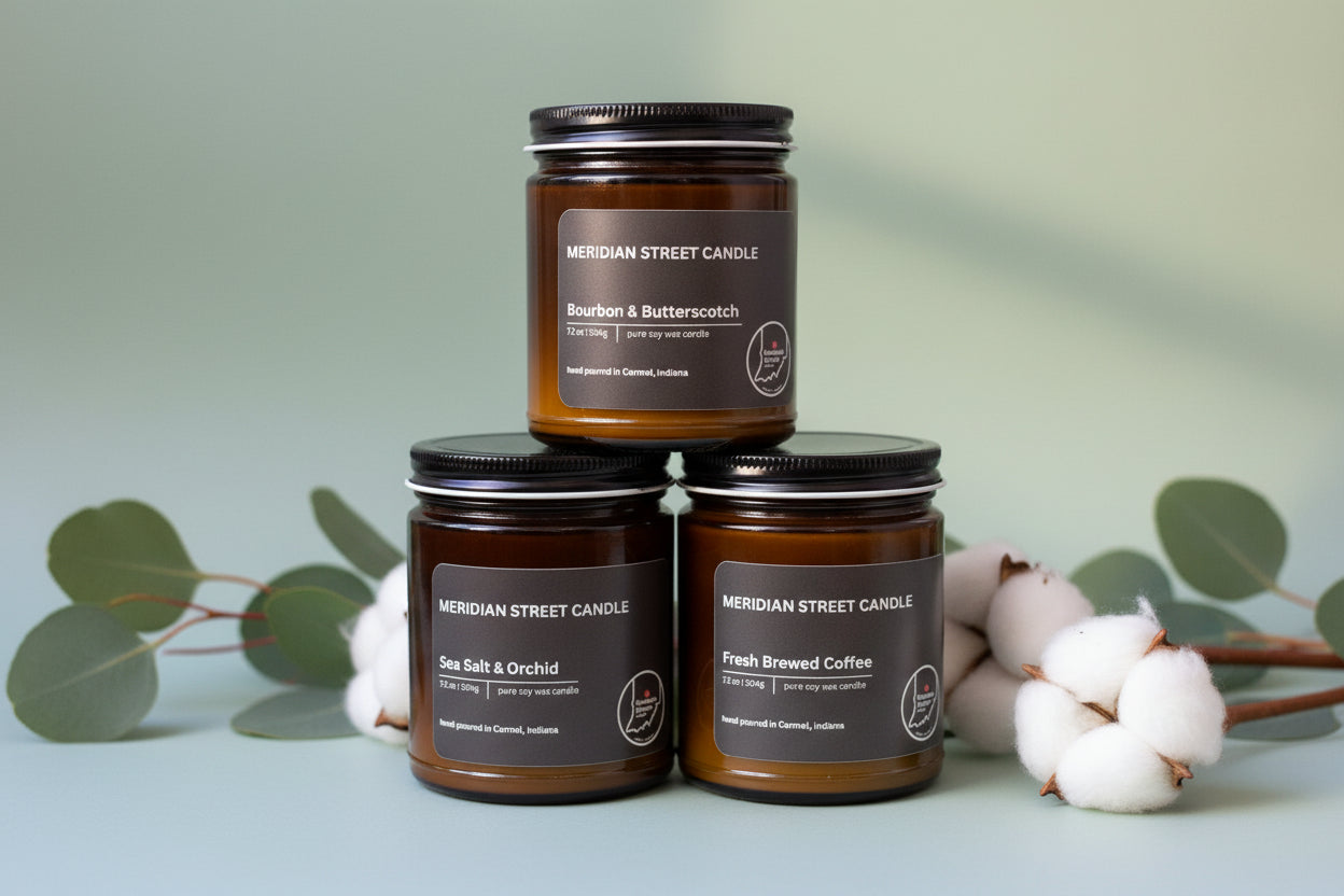 Three candles from Meridian Street Candle on a light blue background with cotton and eucalyptus leaves.