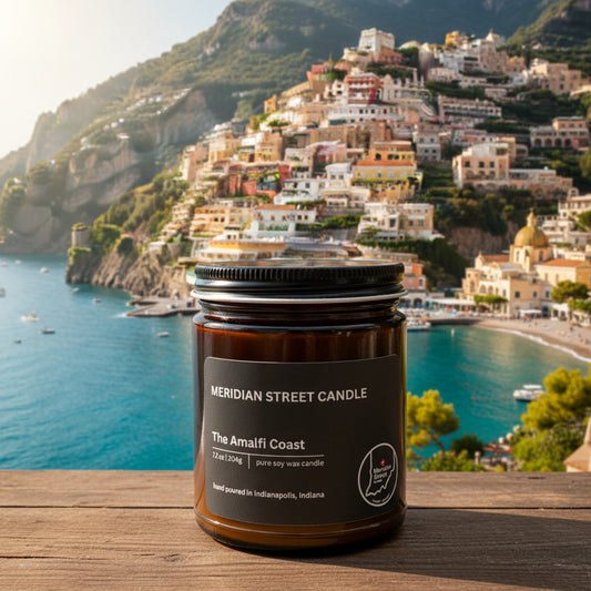 Meridian Street Candle jar labeled 'The Amalfi Coast' on a sunny background with hoses on a hill. 